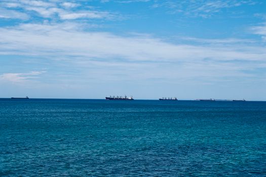 Cum îți influențează certificatul STCW șansele de angajare maritimă în august 2026? 3 Multiple cargo ships floating calmly on the open sea under a clear blue sky.