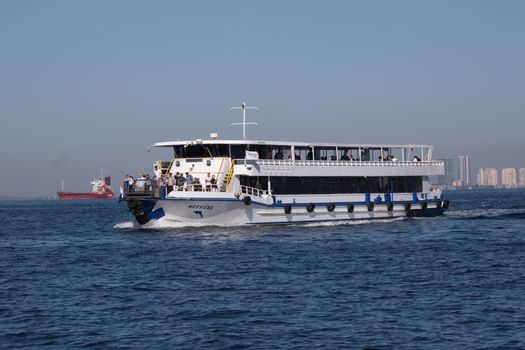 A bustling passenger ferry sails across the İzmir Gulf under clear skies.