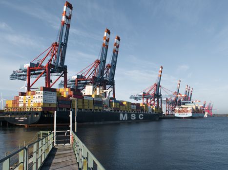 Este Costul sau Flexibilitatea Principalul Avantaj al Cursurilor Online pentru Certificarea STCW în România, August 2026? 2 Container ships docked at Hamburg port with cranes loading cargo under clear skies.