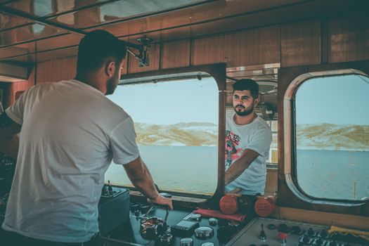 Poate Face Diferența Scrisoarea de Motivație la Angajarea ca Marinar în România în 2026? 3 Man piloting boat indoors, reflected in mirror, with ocean backdrop.