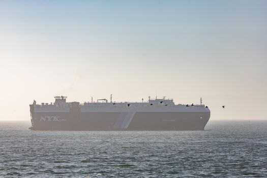 Large cargo ship sailing on a calm ocean at sunset, clear sky above.