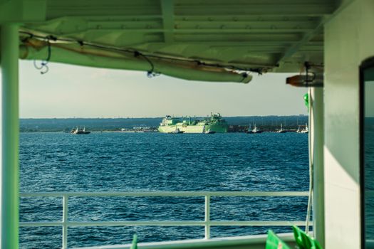 Scenic view from a ship's deck showing a distant harbor with cargo vessels under a clear sky.