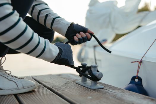 Top 5 Cerințe Pentru a Deveni Master Seaman în 2026 3 Person tying a black rope around a cleat on a yacht deck, wearing gloves.
