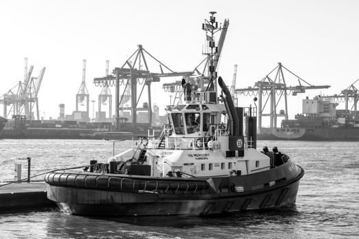Top 5 Oportunități de Angajare ca Ofițer Secund pe Nave Comerciale în România, August 2026 4 Black and white photo of a tugboat in Hamburg harbor with cranes and ships in the background.