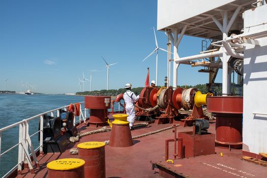 Sailor managing equipment on a ship with offshore wind turbines in the background under a clear blue sky.