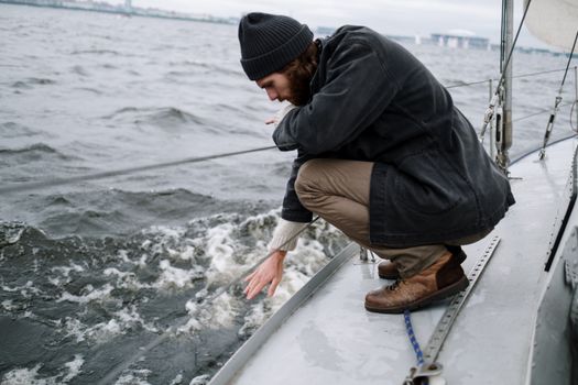 A thoughtful sailor crouches aboard a yacht on a cloudy day.