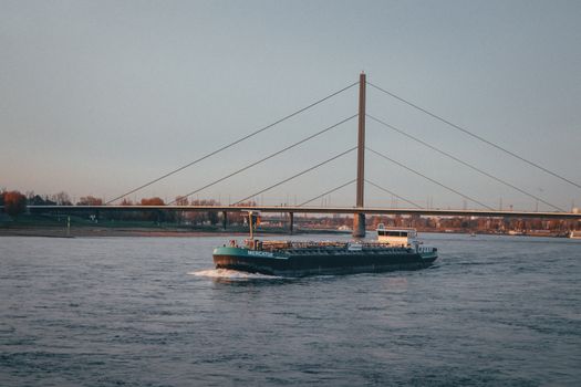 Top 7 Companii de Shipping din România care Revoluționează Formarea Profesională pentru Certificările STCW 2 A cargo vessel passes under a modern suspension bridge on a tranquil river.