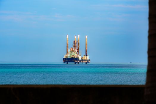 Distant view of an offshore oil rig in a calm, blue ocean under a clear sky.