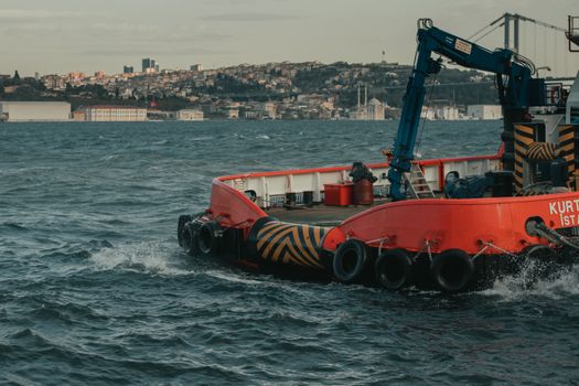 Modern big black crane and wheels on ship in bay next to settlement on mountain slope