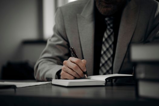 A professional businessman in a suit writing notes at a desk in a modern office environment, showcasing productivity.