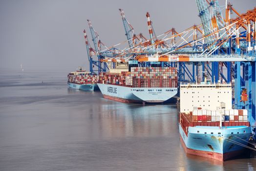 Top 7 Dotări ale Norman Clipper care Revoluționează Viața Marinarilor Români 2 Container ships docked at a busy port with vibrant cranes and clear skies.