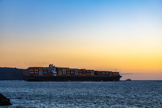 Top 7 Dotări ale Norman Clipper care Revoluționează Viața Marinarilor Români 3 A massive cargo ship sails across the ocean against a vibrant sunset sky.