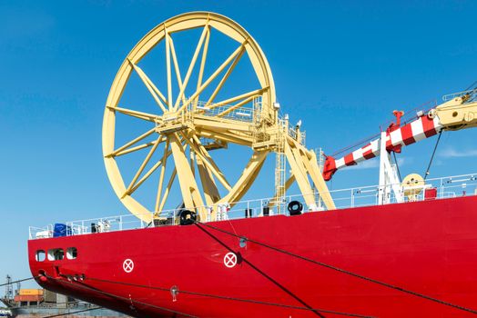 Vibrant red ship with striking yellow machinery docked in Bremerhaven harbor under a clear blue sky.